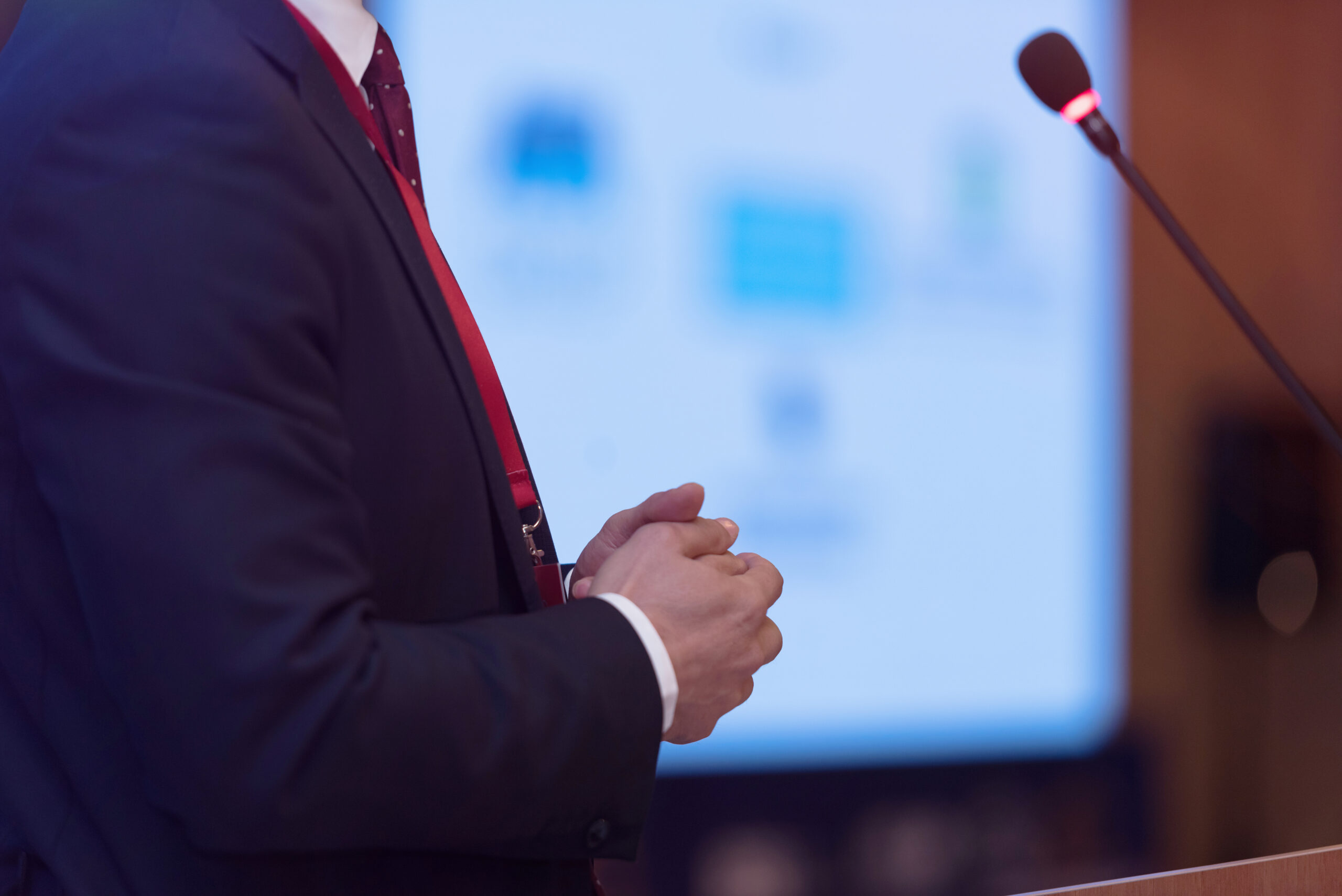 Businessman standing at a podium with blurred presentation in the background.