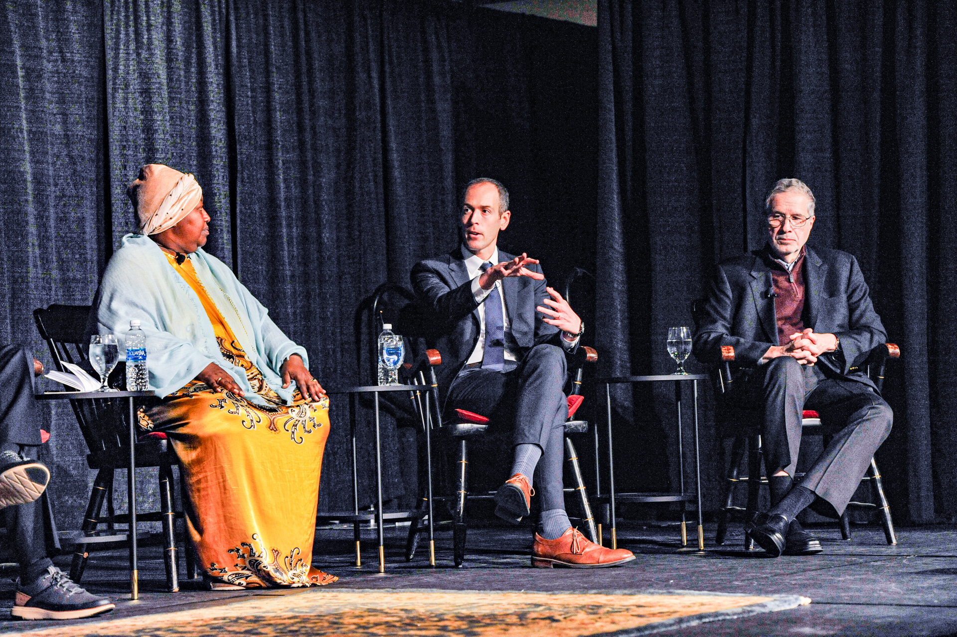 Three speakers sitting on stage engaged in a conversation.